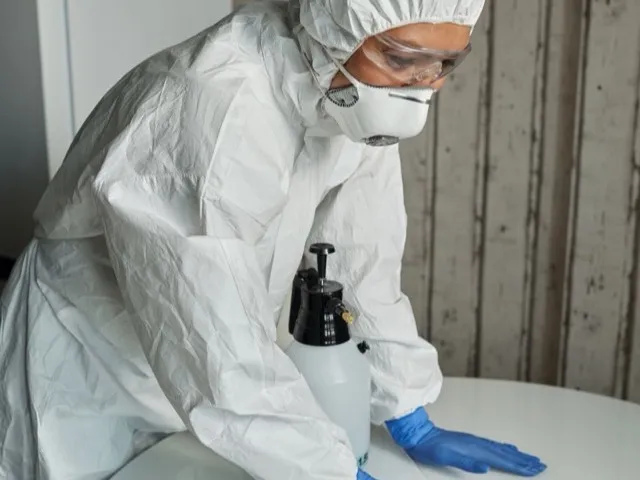 Szakember védőfelszerelésben felületet fertőtlenít spray-vel